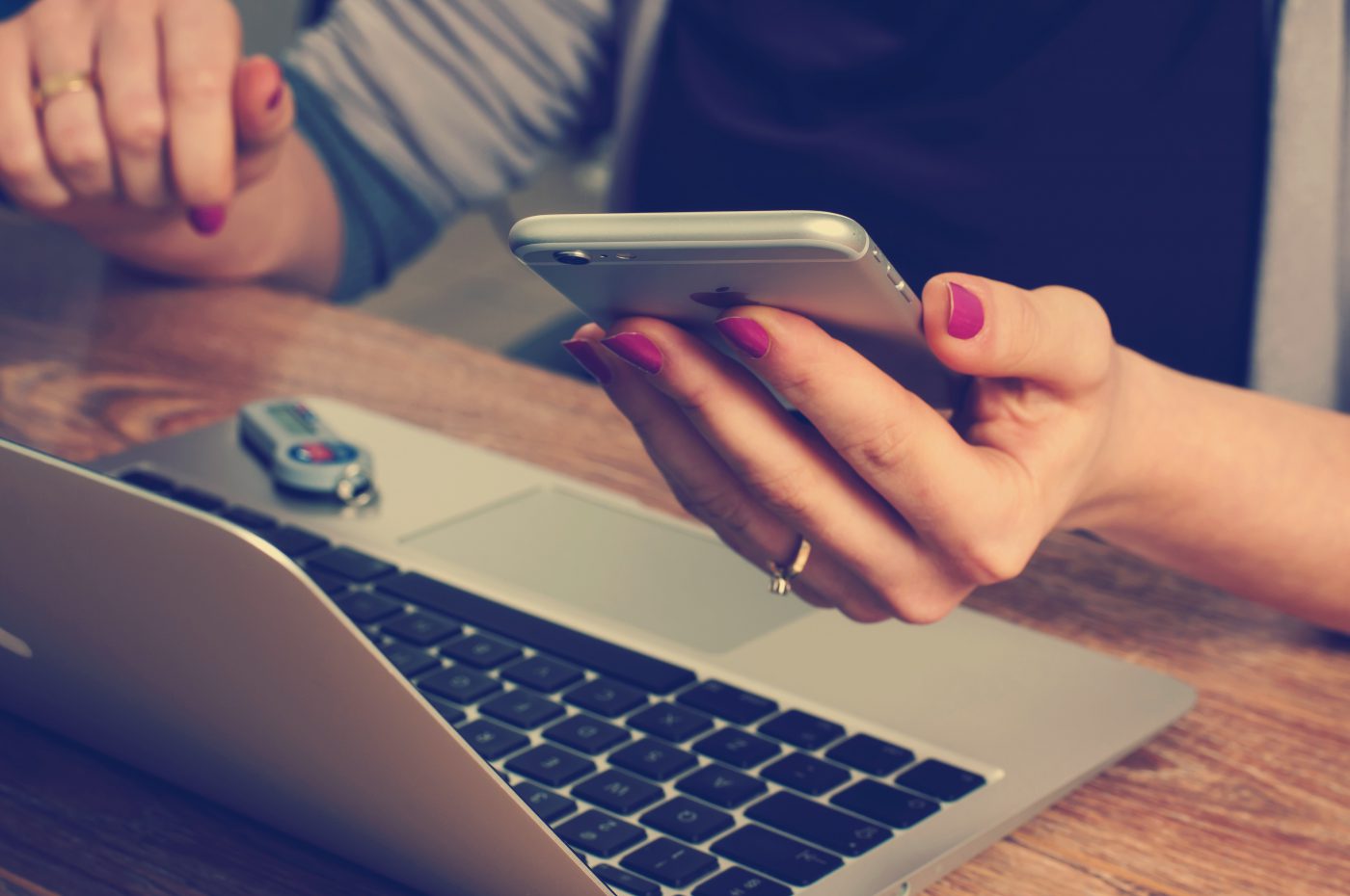 Woman at desk with laptop viewing iphone